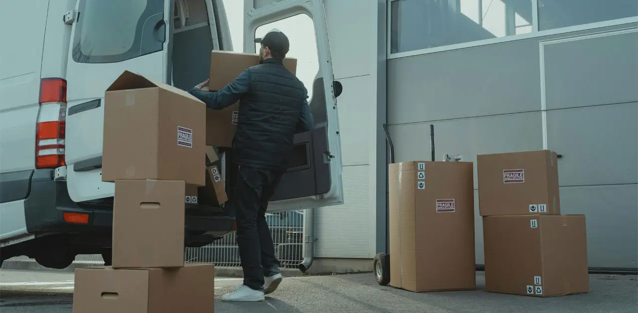 A Man Is Loading Cardboard Boxes Into The Back Of A Van, Preparing For Transportation
