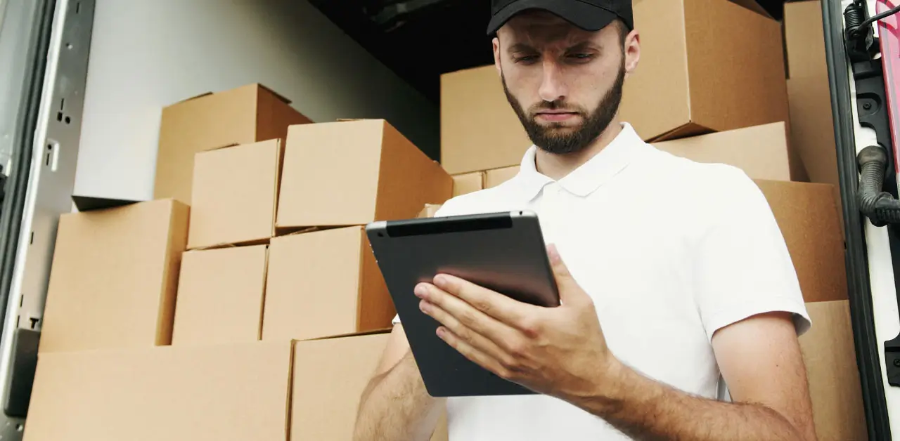 A Man In A White Shirt And Hat Stands Holding A Tablet, Appearing Attentive To The Screen