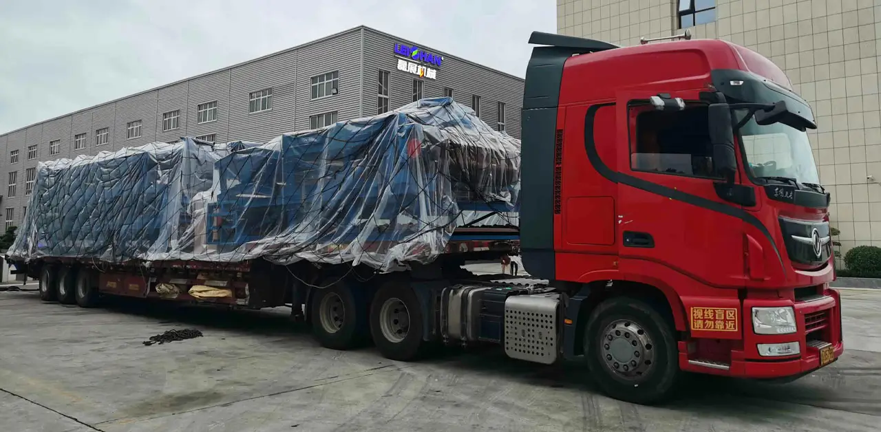 A Large Truck Carrying A Sizable Container On Its Back, Parked On A Street With Clear Blue Skies In The Background