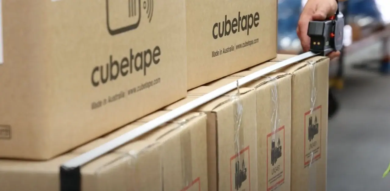 A Hand Grips A Box Adorned With A Bright Green Sticker