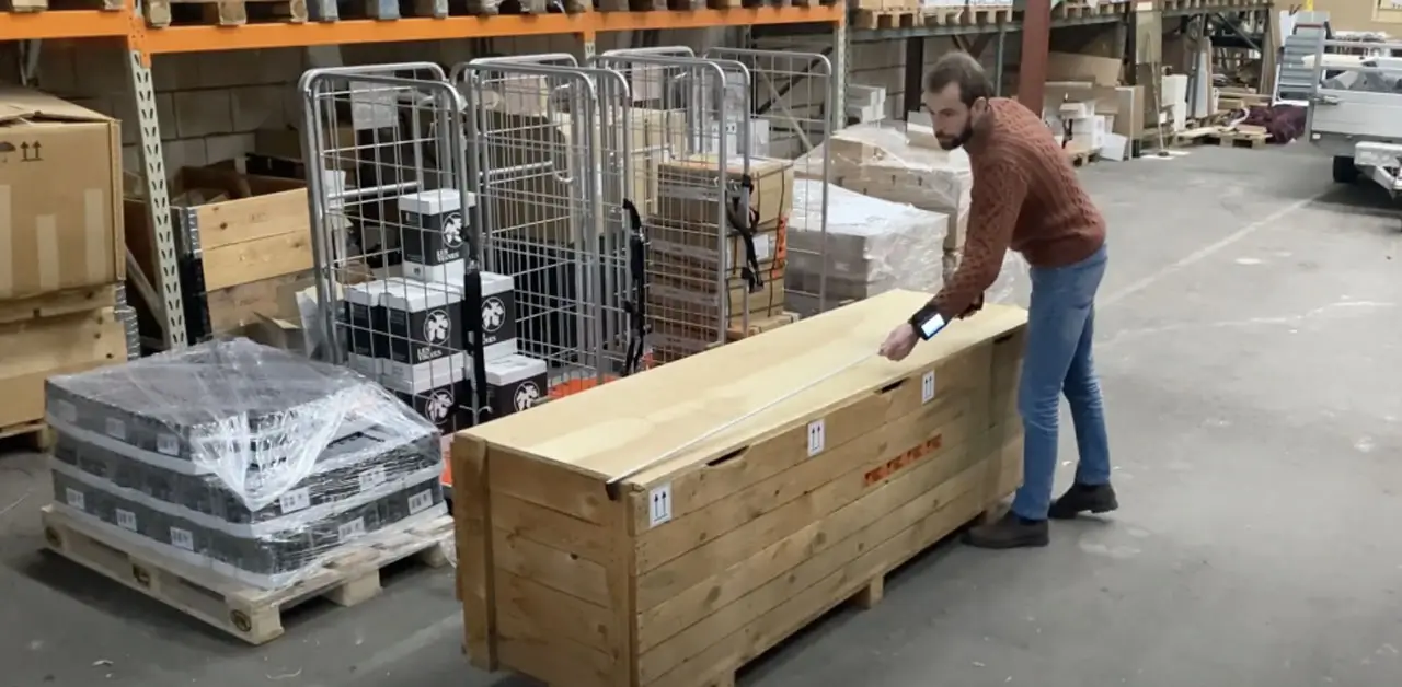 A Man Uses A Tool To Lift And Move A Large Wooden Box In A Workshop Setting