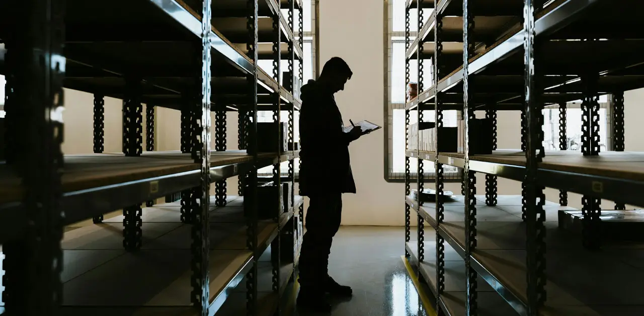 A Person Stands In A Warehouse Surrounded By Tall Shelves Filled With Various Items, Highlighting The Storage Environment