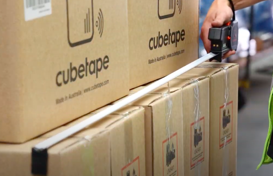 A Worker Measures Boxes With A Tape Measure, Ensuring Accurate Dimensions For Packing Or Shipping Purposes