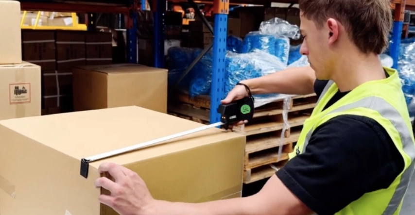 A Man Measures Boxes With A Tape Measure, Focusing On The Dimensions For Accurate Sizing