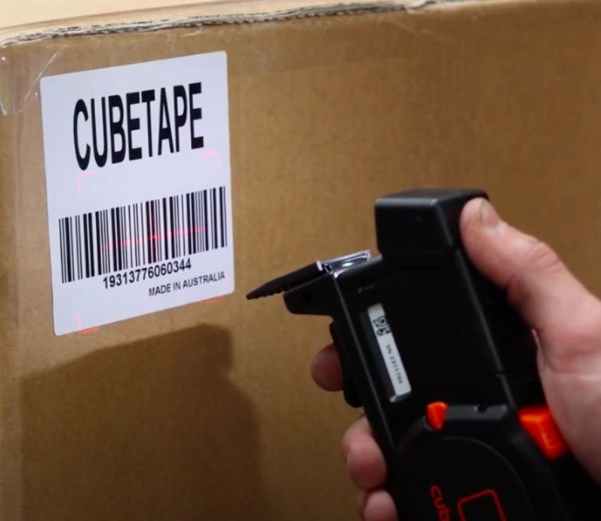 A Person Holds A Barcode Scanner To Scan The Barcode On A Cardboard Box, Focused On The Task At Hand